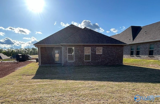 rear view of property featuring brick siding, a yard, and a shingled roof