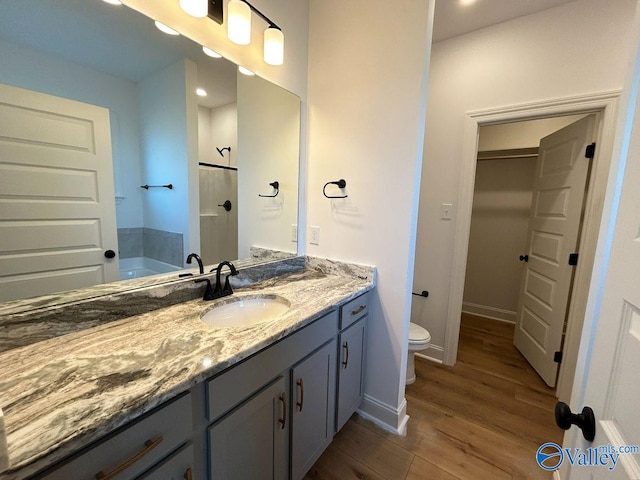bathroom with toilet, baseboards, walk in shower, wood finished floors, and vanity