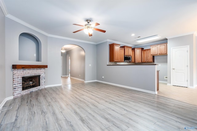 unfurnished living room featuring ornamental molding, ceiling fan, a fireplace, and light hardwood / wood-style flooring