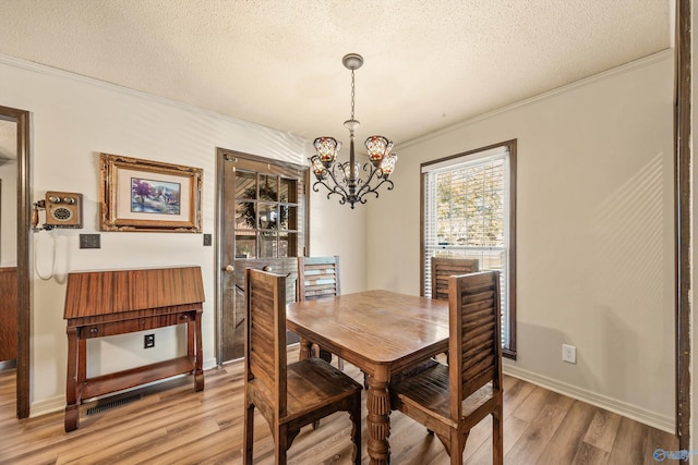 dining area with a chandelier, a textured ceiling, light wood-type flooring, and crown molding