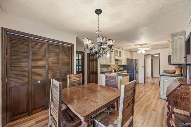 dining area featuring sink, crown molding, light hardwood / wood-style floors, a textured ceiling, and ceiling fan with notable chandelier