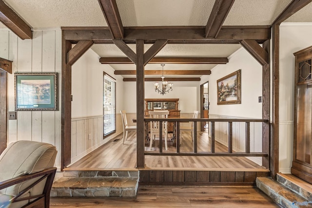 interior space featuring a chandelier, beamed ceiling, wood-type flooring, and a textured ceiling