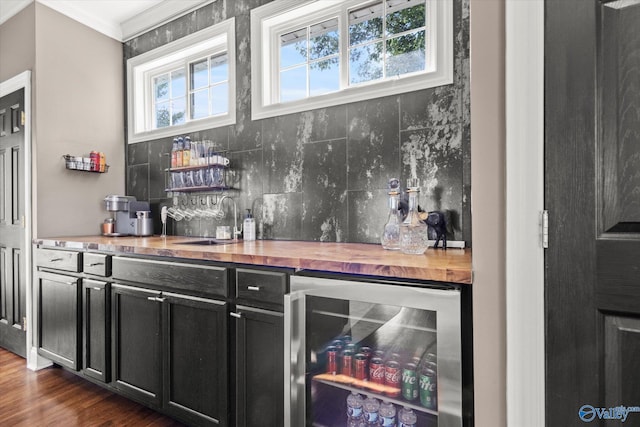 bar with butcher block counters, a healthy amount of sunlight, beverage cooler, and dark hardwood / wood-style flooring