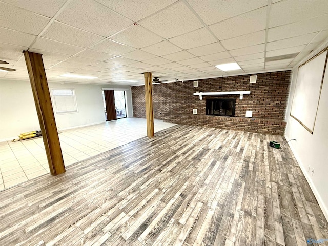 basement featuring a brick fireplace, brick wall, a paneled ceiling, and wood finished floors