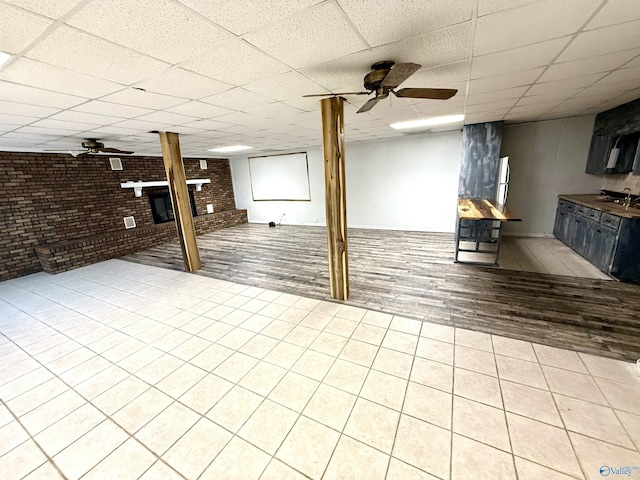 finished below grade area featuring a brick fireplace, brick wall, ceiling fan, a drop ceiling, and a sink