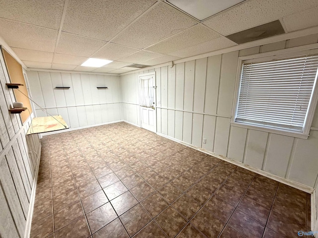 spare room featuring tile patterned floors, a decorative wall, and a paneled ceiling