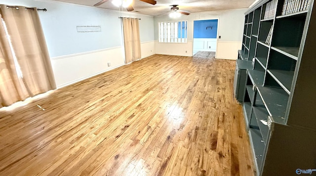 empty room with a wainscoted wall, wood finished floors, and ceiling fan