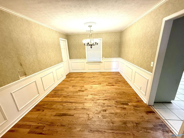 unfurnished dining area with crown molding, a chandelier, a wainscoted wall, wood finished floors, and a textured ceiling