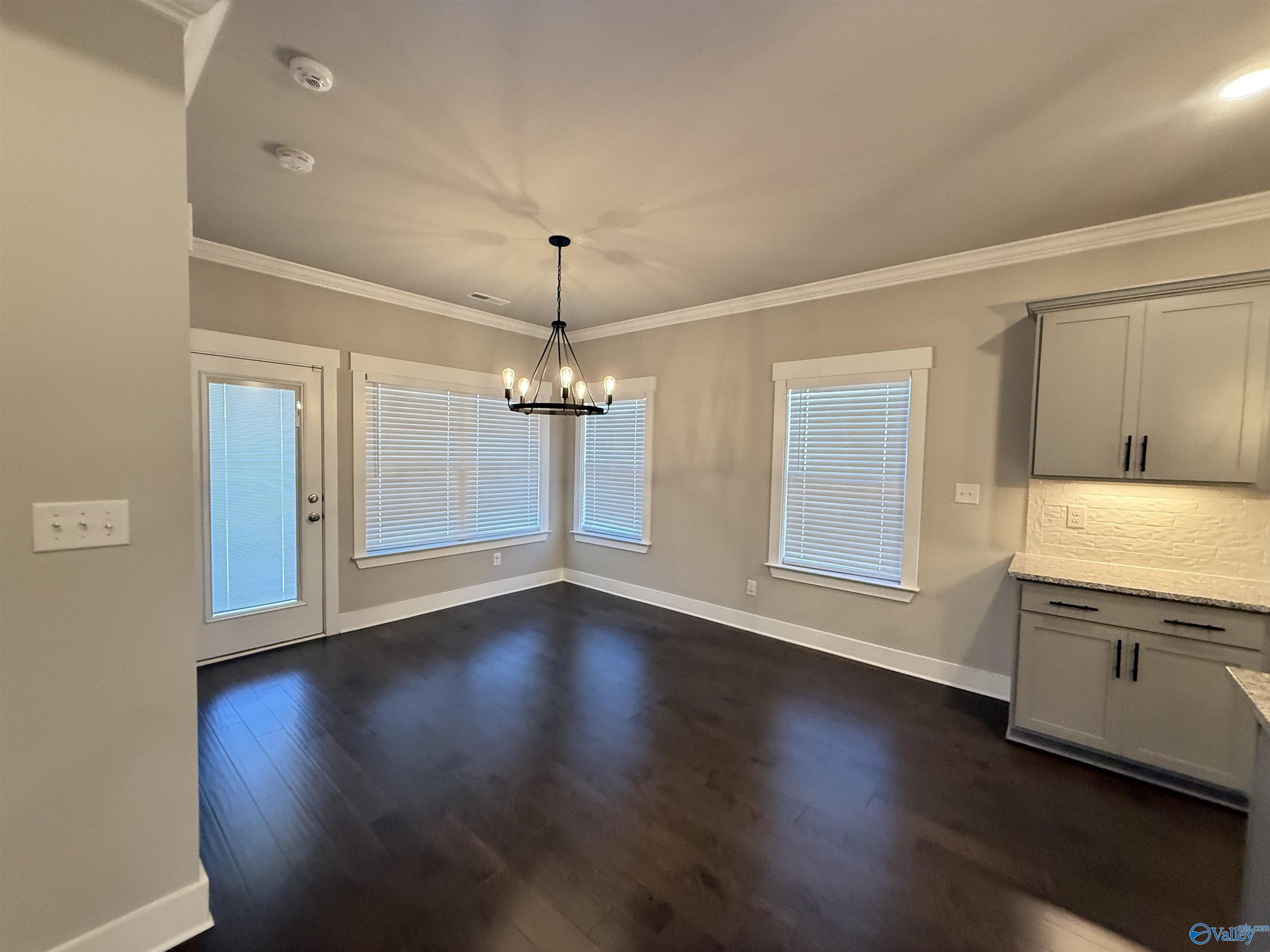 unfurnished dining area with dark wood-style floors, baseboards, a notable chandelier, and crown molding