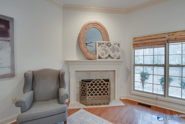 sitting room featuring a tile fireplace, light wood-type flooring, and ornamental molding