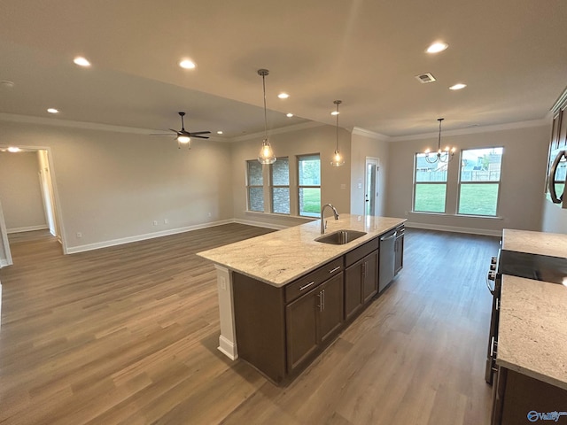 kitchen featuring pendant lighting, sink, crown molding, light stone countertops, and a center island with sink