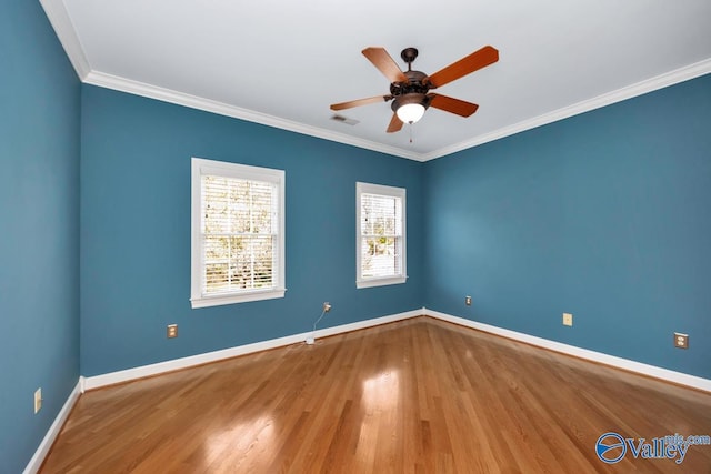 empty room with baseboards, ornamental molding, visible vents, ceiling fan, and wood finished floors