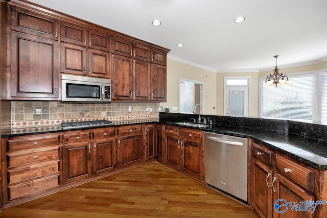 kitchen with light wood-style floors, ornamental molding, a chandelier, a sink, and stainless steel appliances