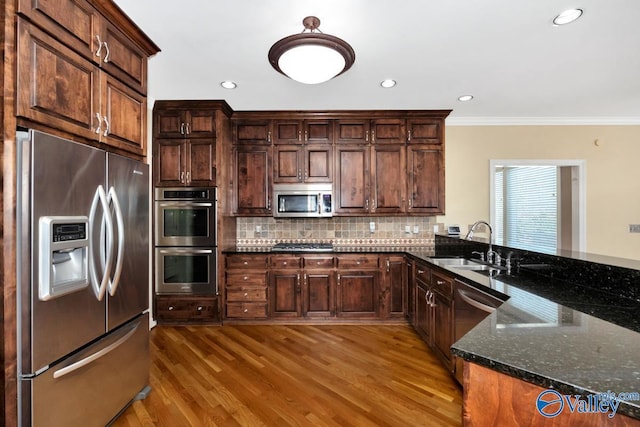 kitchen with tasteful backsplash, dark stone countertops, appliances with stainless steel finishes, a sink, and wood finished floors