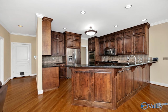 kitchen with crown molding, wood finished floors, backsplash, and stainless steel appliances
