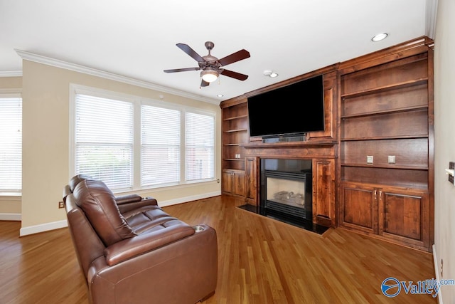 living area with ceiling fan, a fireplace with flush hearth, ornamental molding, wood finished floors, and baseboards