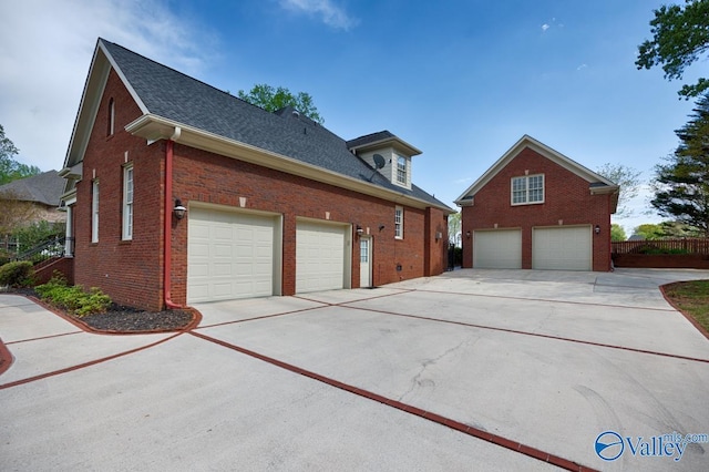view of side of home featuring concrete driveway, a detached garage, fence, and brick siding