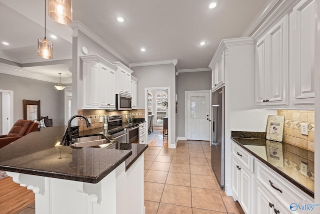 kitchen featuring tasteful backsplash, appliances with stainless steel finishes, a sink, white cabinetry, and a kitchen breakfast bar
