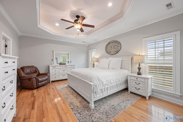bedroom with ornamental molding, visible vents, a raised ceiling, and light wood-style floors