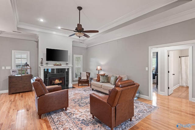 living room with ceiling fan, light wood-style floors, a tiled fireplace, and ornamental molding
