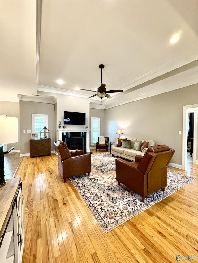 living room featuring a tile fireplace, a ceiling fan, light wood-style flooring, and crown molding