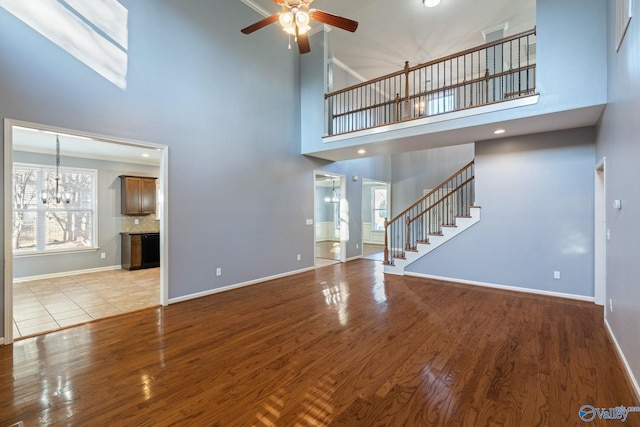 unfurnished living room with light hardwood / wood-style floors, high vaulted ceiling, and ceiling fan with notable chandelier