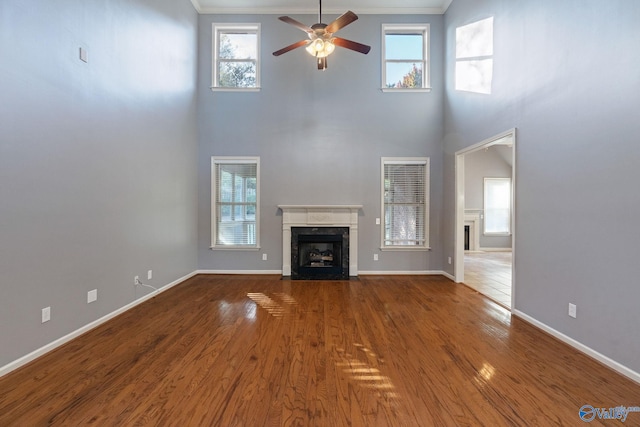 unfurnished living room featuring a healthy amount of sunlight, a towering ceiling, ornamental molding, and hardwood / wood-style floors