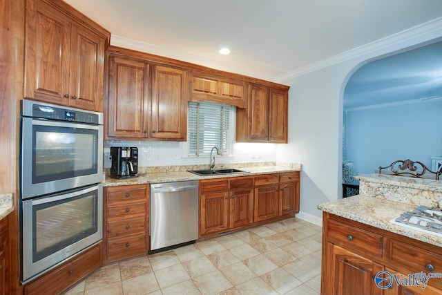 kitchen featuring light stone counters, a sink, appliances with stainless steel finishes, brown cabinetry, and crown molding