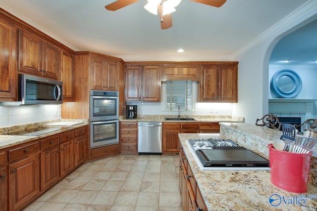 kitchen featuring stainless steel appliances, a sink, ornamental molding, brown cabinets, and decorative backsplash