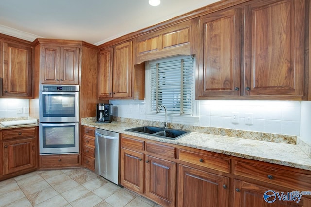 kitchen featuring brown cabinetry, a sink, light stone countertops, stainless steel appliances, and backsplash