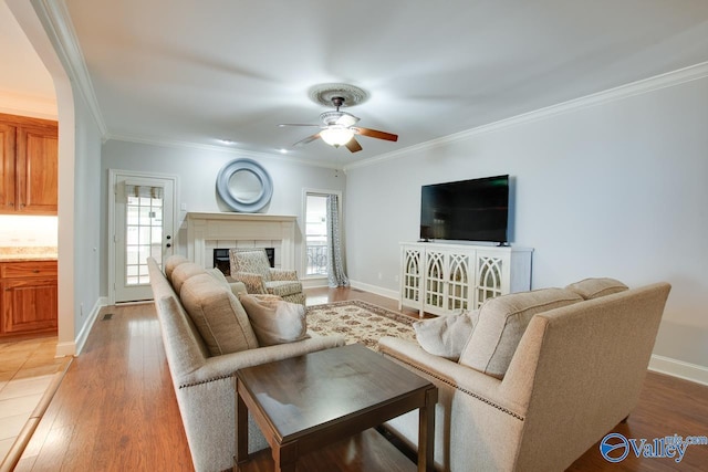 living area with ornamental molding, light wood-type flooring, a fireplace, and ceiling fan