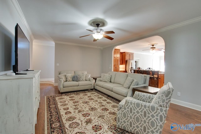 living room with arched walkways, crown molding, light wood finished floors, and ceiling fan