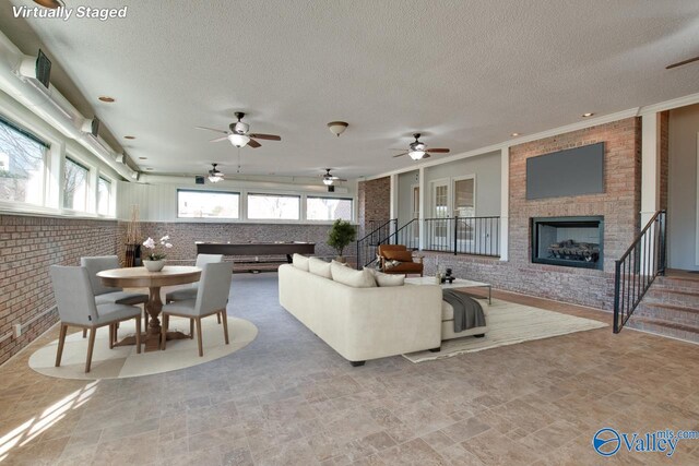 living area featuring a brick fireplace, brick wall, stairs, and a textured ceiling