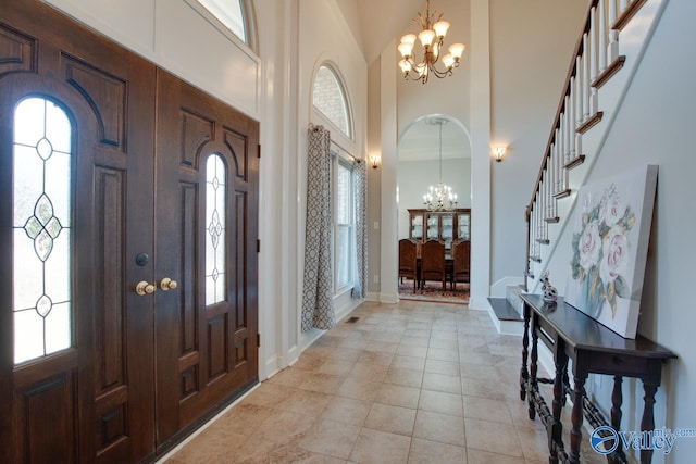 entrance foyer featuring arched walkways, light tile patterned floors, a towering ceiling, a chandelier, and stairs