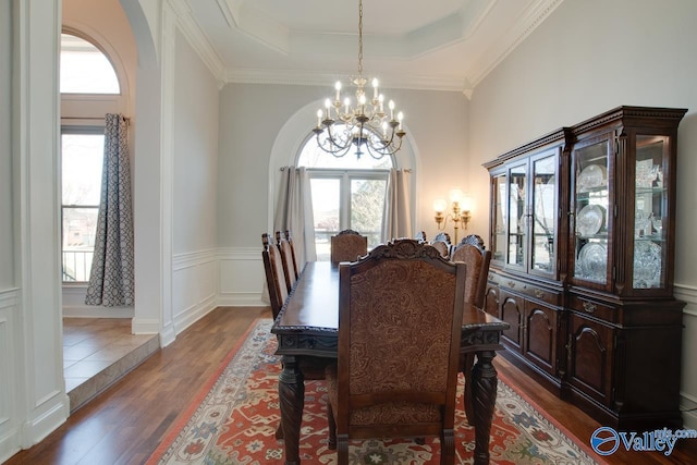 dining space with a tray ceiling, arched walkways, a notable chandelier, ornamental molding, and wood finished floors