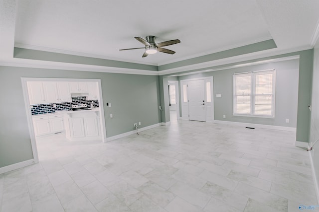 unfurnished living room with ornamental molding, baseboards, a ceiling fan, and a raised ceiling