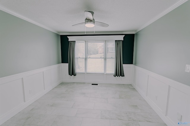 empty room featuring ceiling fan, ornamental molding, and a wainscoted wall