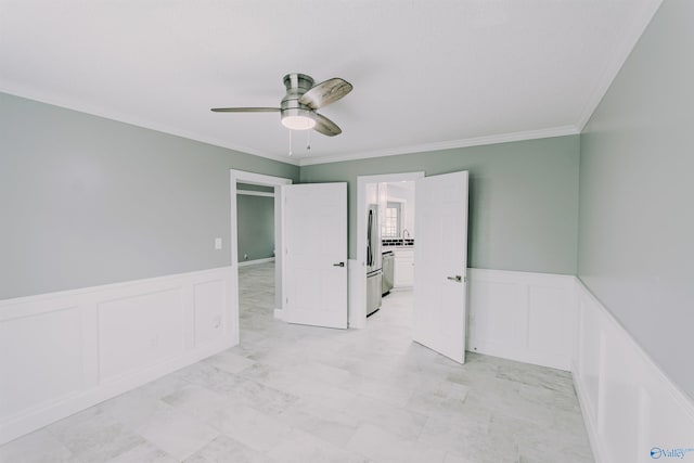 unfurnished room with a decorative wall, ornamental molding, a ceiling fan, and a wainscoted wall