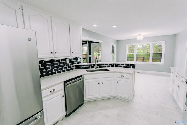kitchen featuring tasteful backsplash, a peninsula, light countertops, a sink, and stainless steel appliances