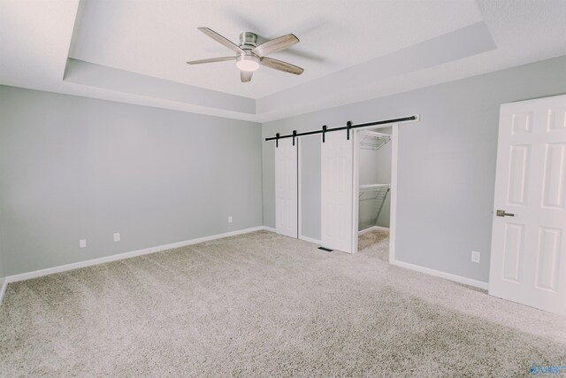 unfurnished bedroom featuring a tray ceiling, light colored carpet, and a barn door