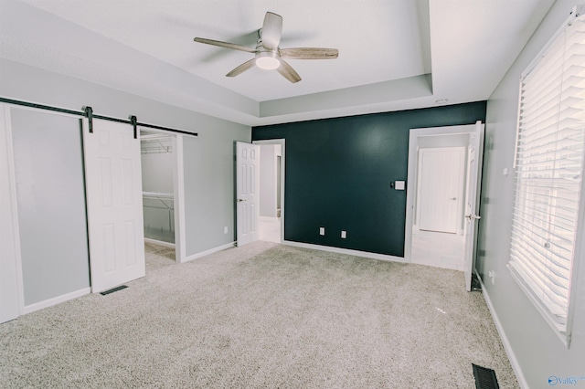 unfurnished bedroom with carpet, visible vents, and a barn door