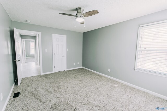unfurnished bedroom featuring a textured ceiling, a ceiling fan, visible vents, carpet flooring, and baseboards