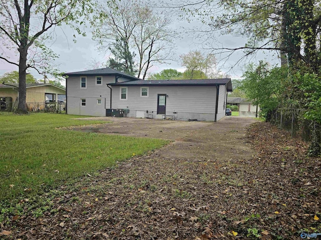rear view of property with central AC unit, fence, and a lawn