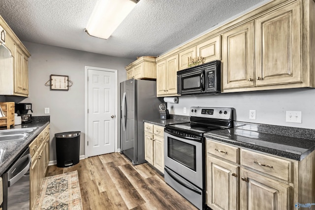 kitchen featuring sink, a textured ceiling, appliances with stainless steel finishes, hardwood / wood-style flooring, and dark stone counters