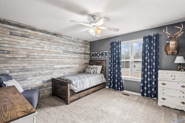 carpeted bedroom featuring ceiling fan, a textured ceiling, and wood walls