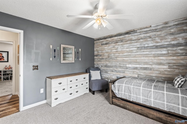 bedroom with ceiling fan, carpet floors, wooden walls, and a textured ceiling