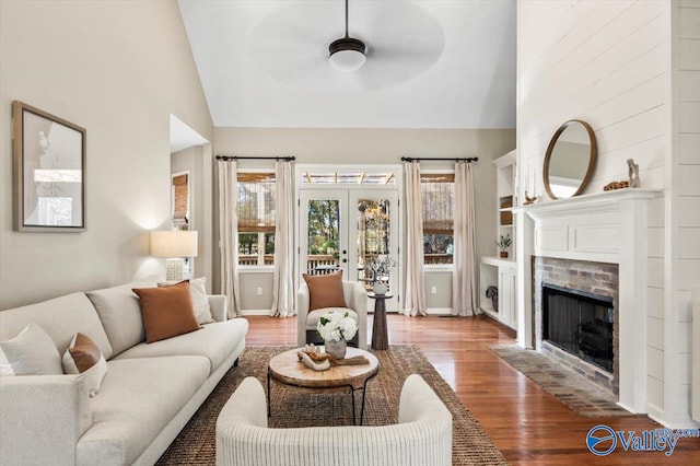 living room featuring french doors, ceiling fan, wood-type flooring, high vaulted ceiling, and a fireplace