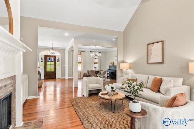 living room featuring lofted ceiling, a chandelier, light wood-type flooring, ornamental molding, and decorative columns