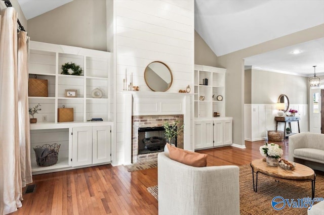 living room featuring a brick fireplace, crown molding, high vaulted ceiling, and light hardwood / wood-style flooring