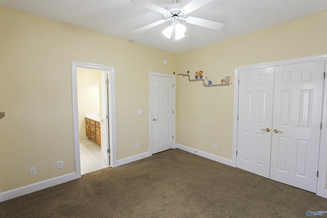 unfurnished bedroom featuring connected bathroom, ceiling fan, a closet, and dark carpet